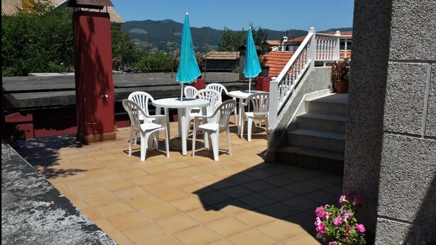 An outdoor patio with white plastic chairs and tables, a red pillar, and a staircase leading to an upper level. - Rincón Do Demo (Nigran)
