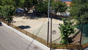A fenced outdoor area with a netted play zone, trees, and a building with a 'HOTEL' sign in the background. - Rincón Do Demo (Nigran)