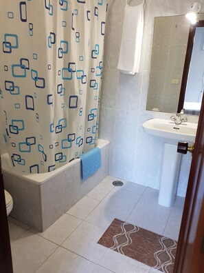 A bathroom with a shower curtain, a sink, a mirror, and a patterned floor mat.