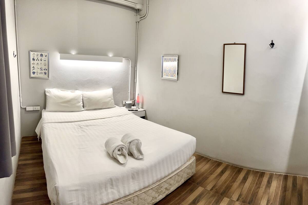 A hotel room with a bed, a bedside table, a nightstand, a wall-mounted TV, and a mirror.