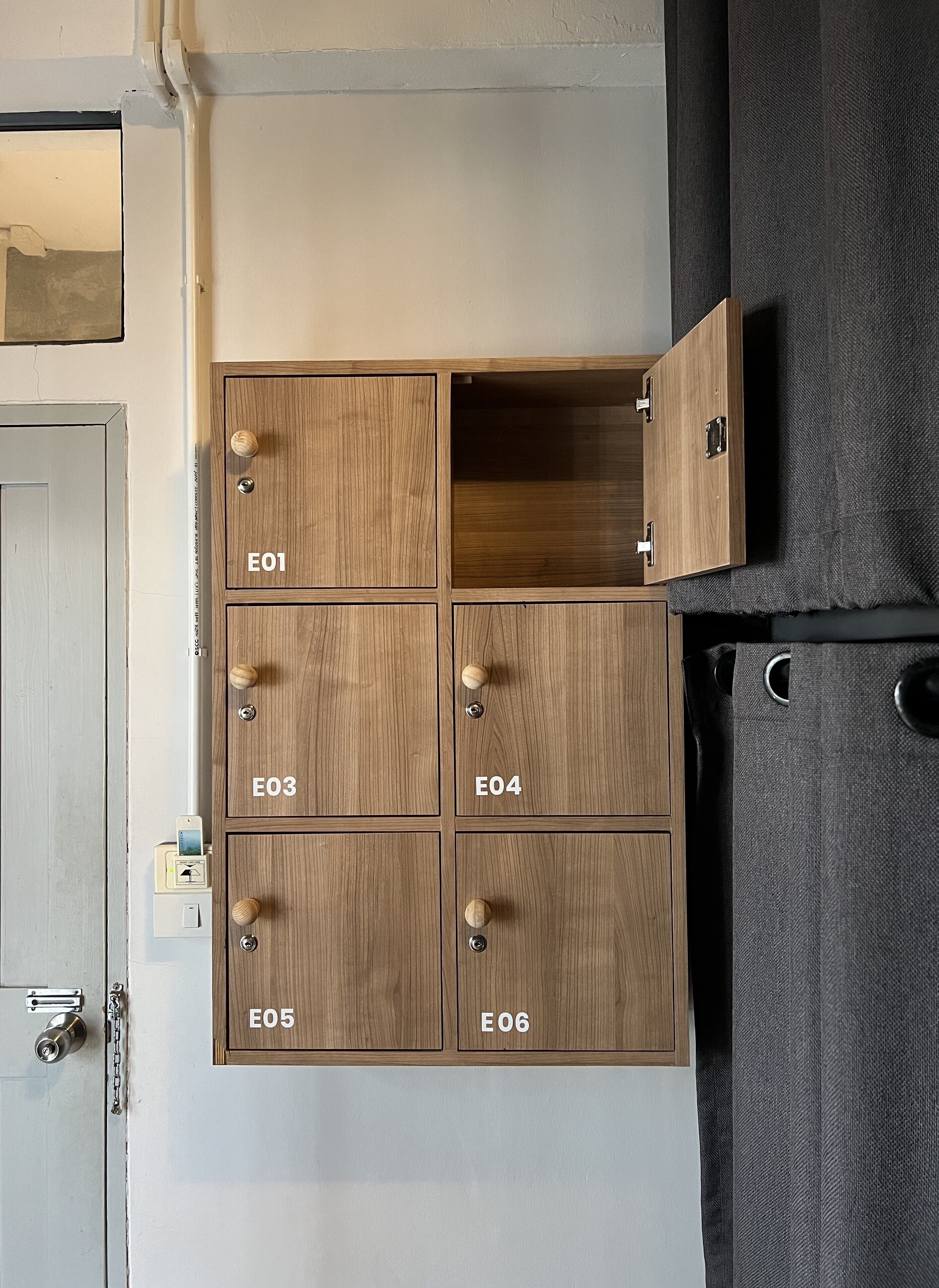 A wooden storage unit with six compartments labeled E01 to E06, a door with a handle, and a light switch.