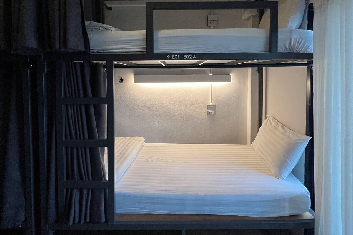 A bunk bed room with a ladder, a control panel above the beds, and a curtain on the left.
