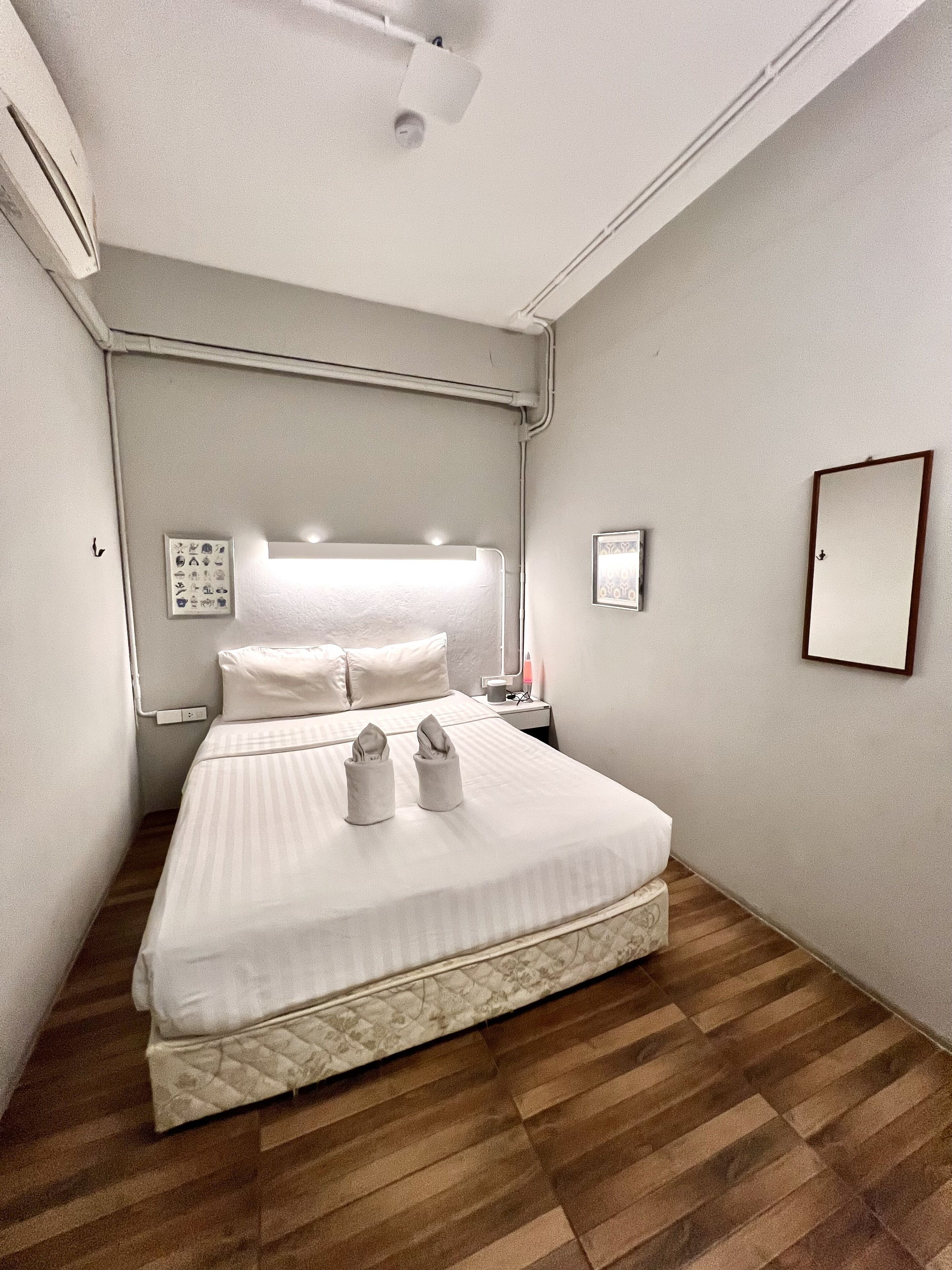 A neatly made bed in a hotel room with a headboard, a bedside table with a lamp, and a wall-mounted mirror.