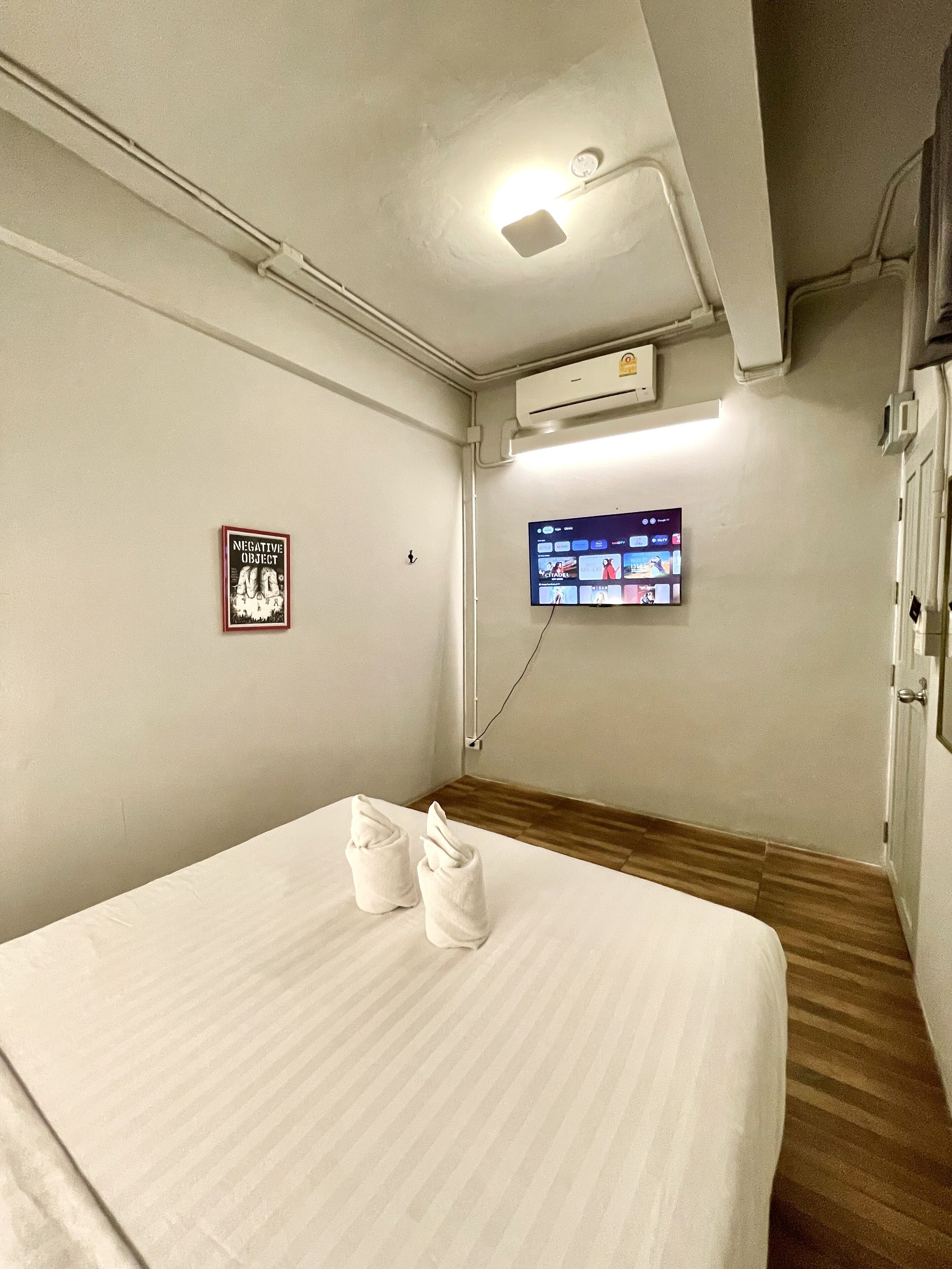 A hotel room with a bed, a wall-mounted TV, an air conditioning unit, and a sign reading "NEGATIVE OBJECT".