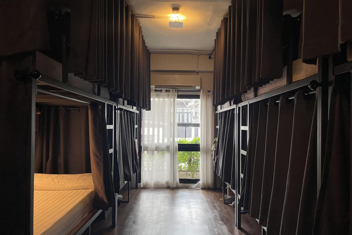 A narrow corridor with bunk beds on either side, leading to a door with a view of greenery outside.