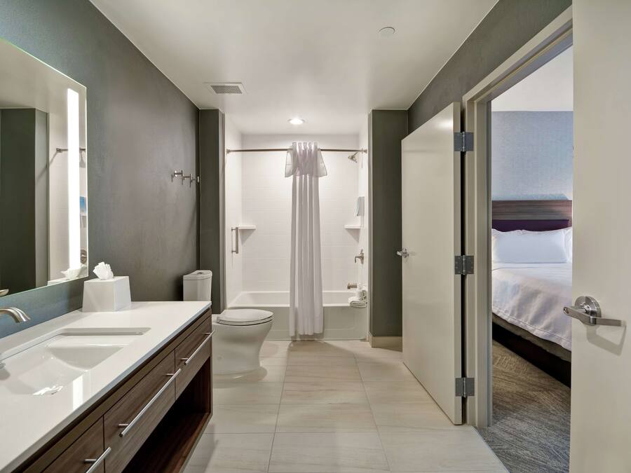 A modern bathroom with a large mirror, two sinks, a toilet, and a shower.