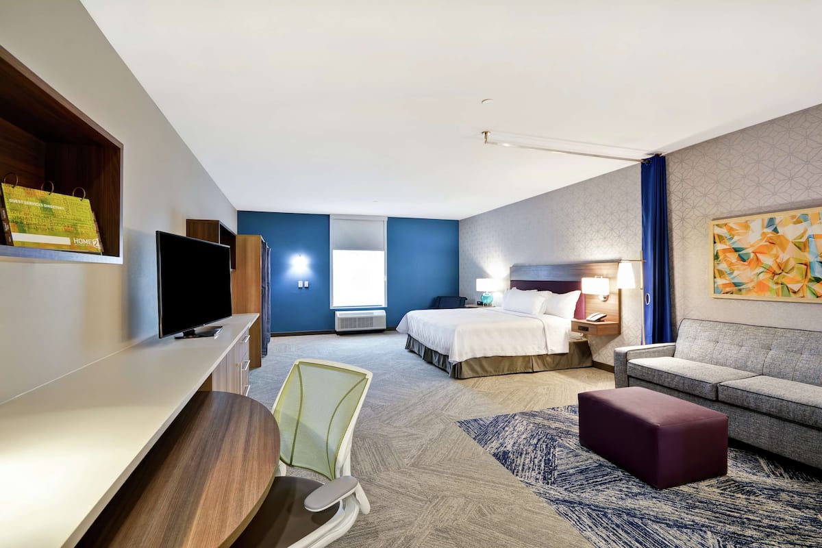 Une chambre d’hôtel avec un lit, un bureau, une télévision, une chaise, un canapé et un tableau au mur.
