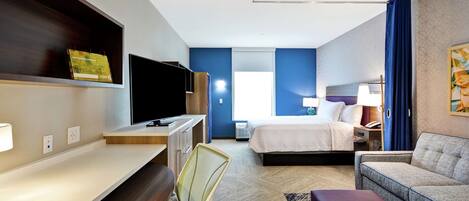 A hotel room with a bed, a desk with a chair, a television, and a sofa.