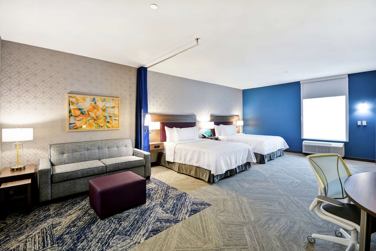 Une chambre d’hôtel avec un canapé gris, deux lits, un bureau et une chaise.