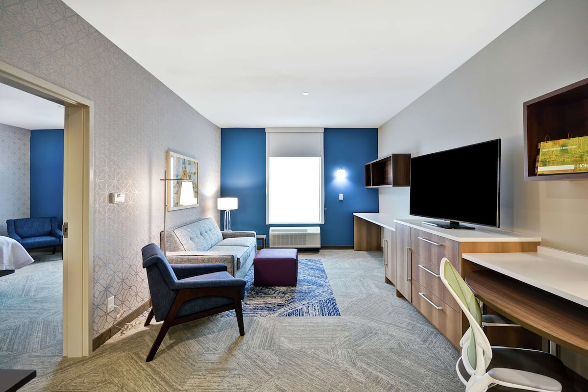 Une chambre d’hôtel moderne dotée d’un espace salon, d’une télévision, d’un bureau et d’un coin salon confortable.