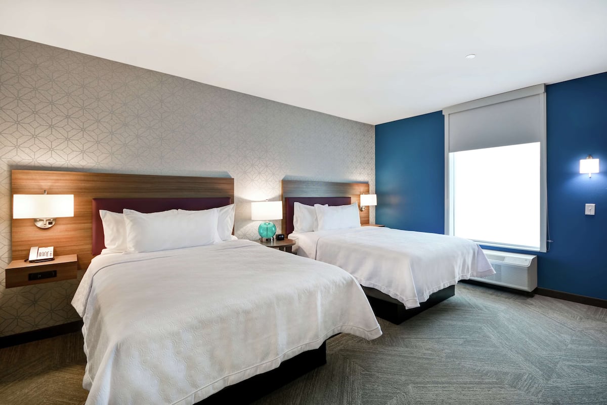 Une chambre d’hôtel avec deux lits, une table de chevet avec une lampe et une grande fenêtre.