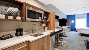 Habitación de hotel pequeña con kitchenette, cama, escritorio y silla.