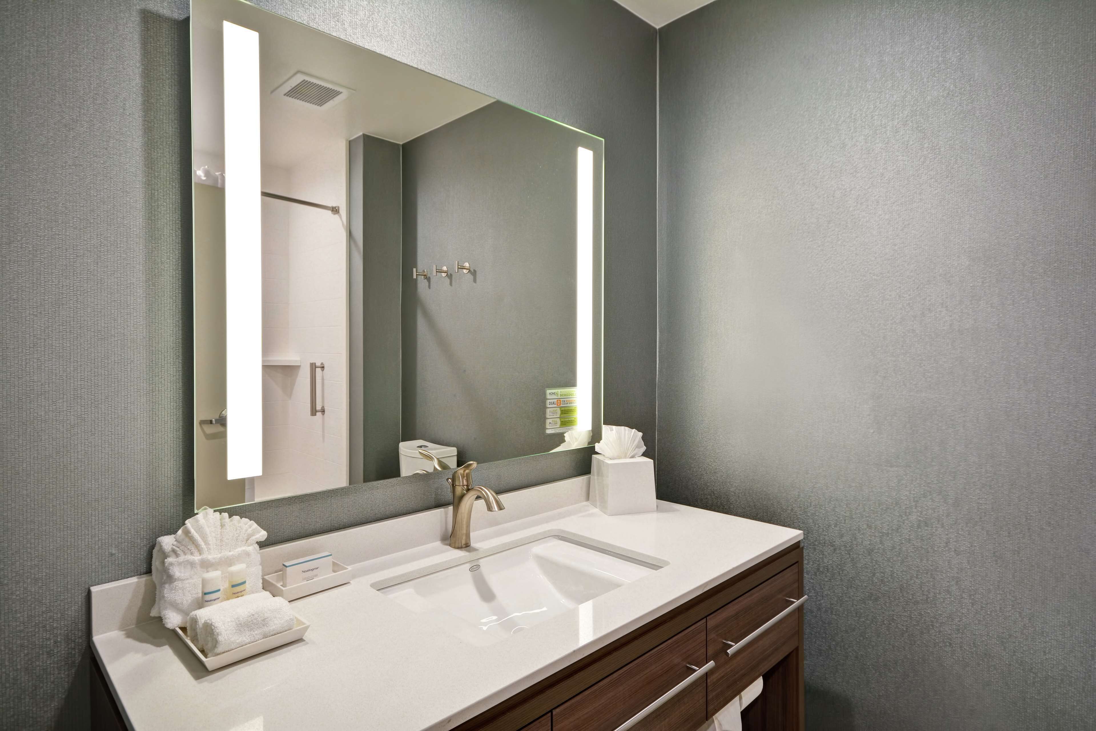 A modern bathroom with a large mirror, a white sink, and a wooden vanity.