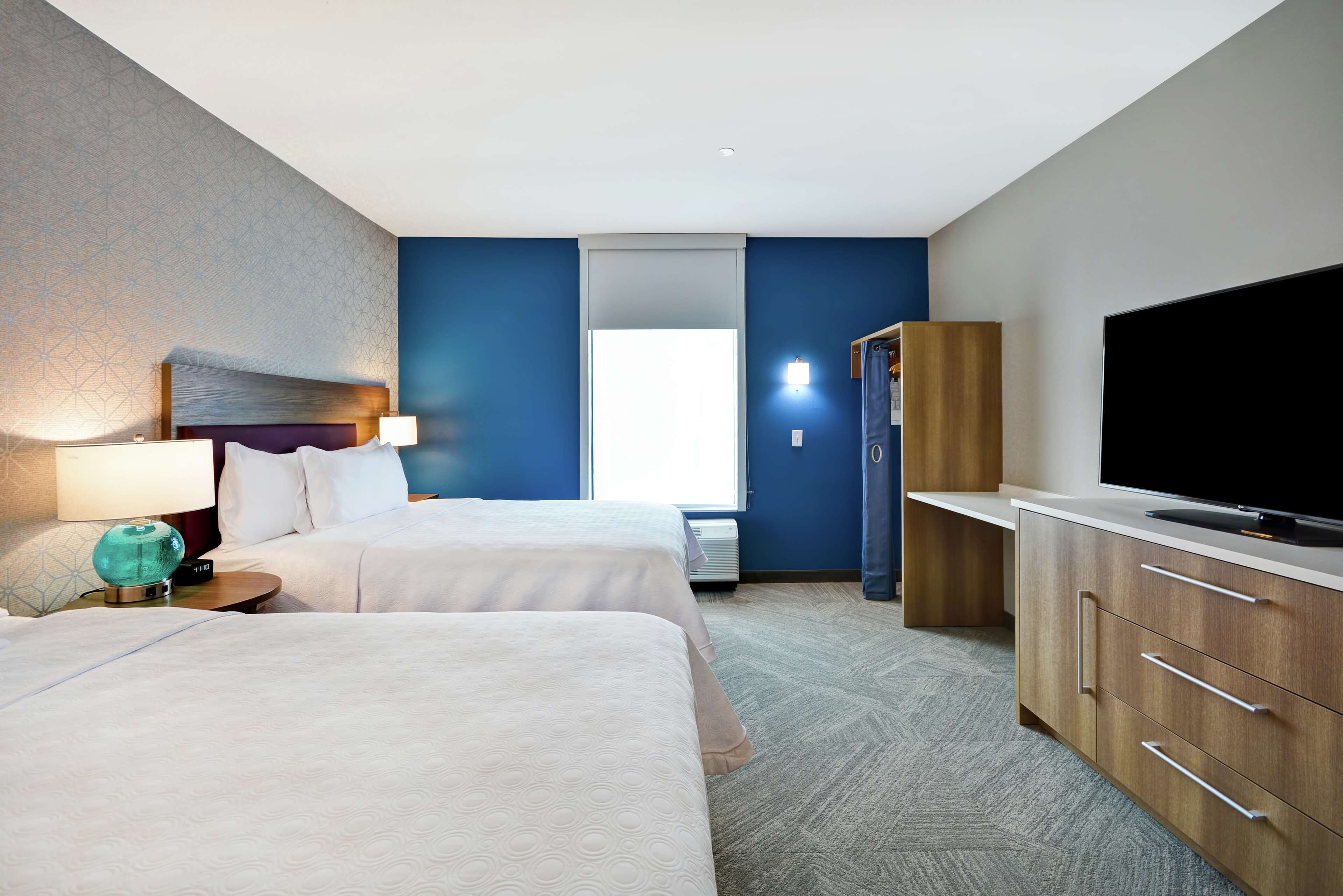 Ein Hotelzimmer mit zwei Betten, einem Fernseher, einem Kleiderschrank und einem Fenster mit Jalousien.