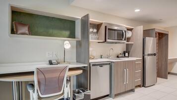 A modern kitchen with a built-in microwave, refrigerator, and dishwasher. There is a dining area with a chair and a table.