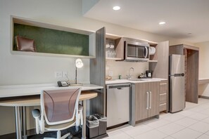 A modern kitchen with a built-in microwave, refrigerator, and dishwasher. There is a dining area with a chair and a table.
