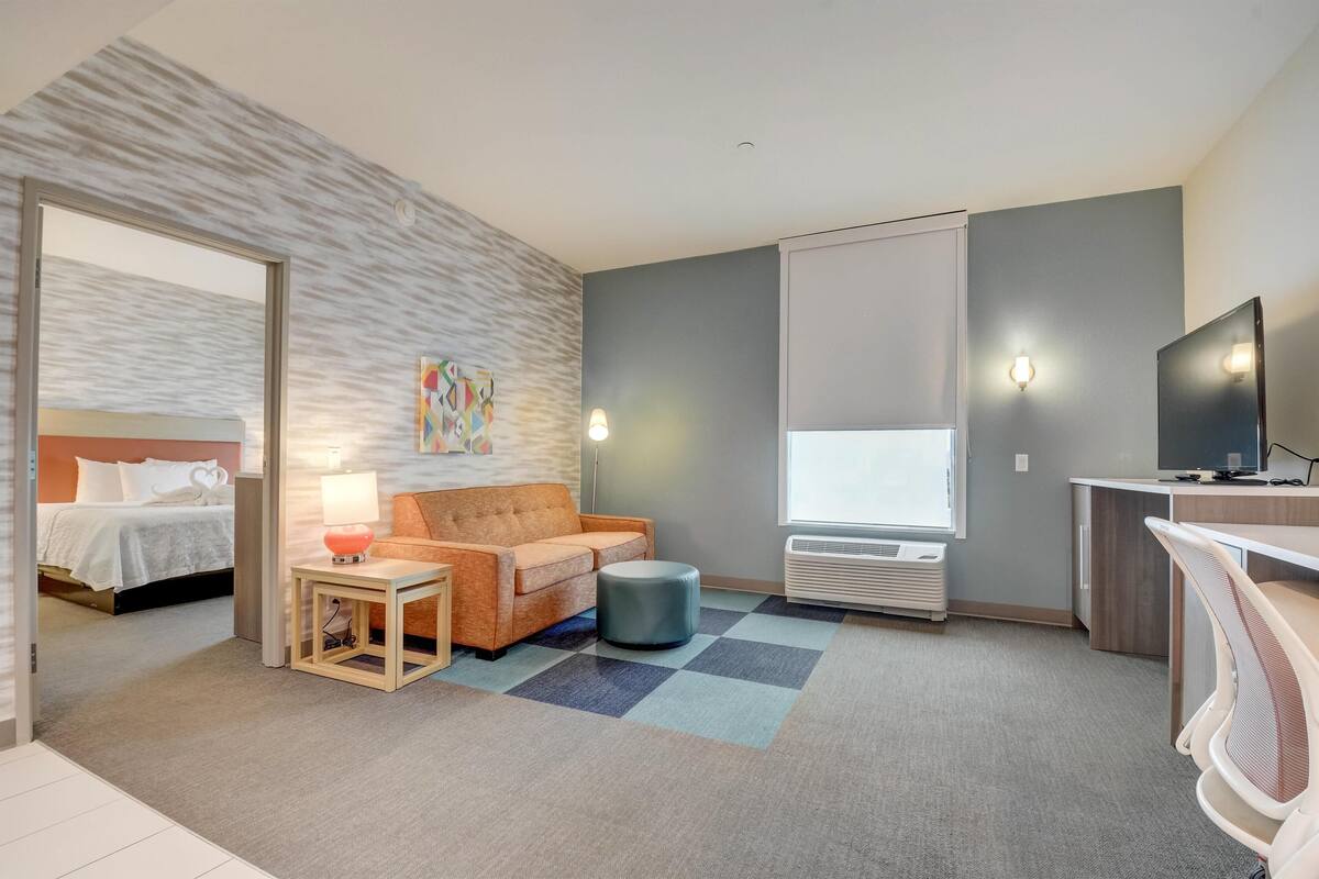 Habitació d'hotel amb un llit, un sofà, una taula petita amb una làmpada, un televisor i una finestra.