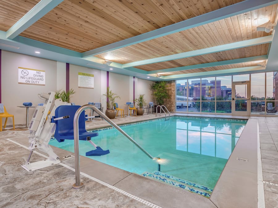 A pool area with a no diving sign, a lifeguard chair, and a view of the cityscape through large windows.