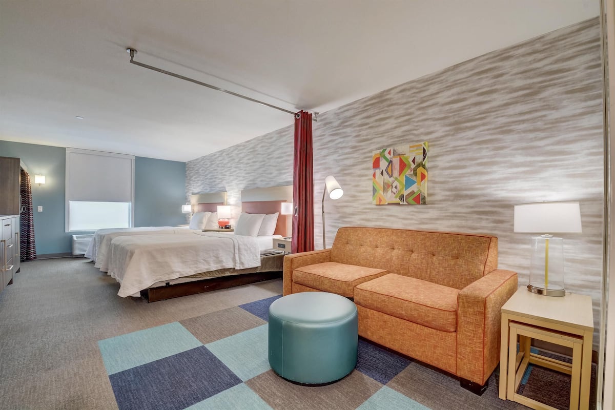 Una habitació d'hotel amb un llit, un sofà, una taula petita, una làmpada i una obra d'art colorida a la paret.
