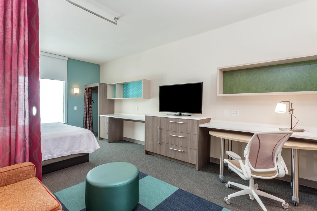 Habitació d'hotel amb llit, escriptori, cadira, televisió i una petita zona de seients.