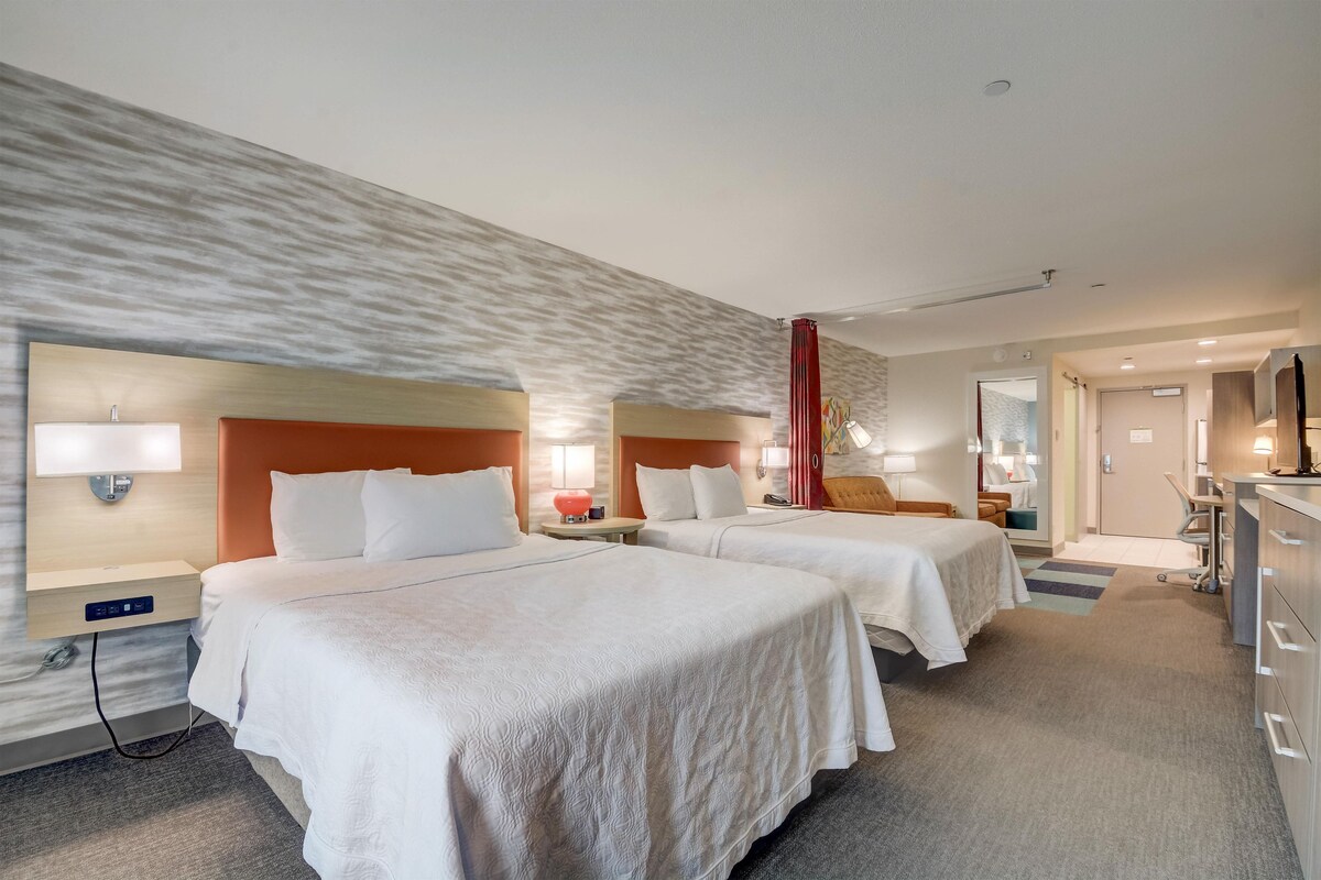 A hotel room with two beds, a desk, a chair, and a TV.