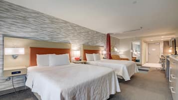 A hotel room with two beds, a desk, a chair, and a TV.
