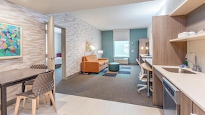 A modern hotel room with a dining area, kitchenette, and a view of the city. - Home2 Suites by Hilton Indianapolis Northwest (Indianapolis)