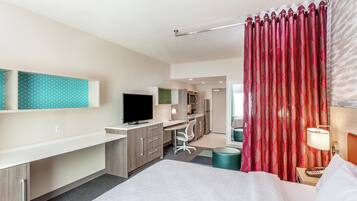 A hotel room with a bed, desk, chair, TV, and a bathroom visible in the background.