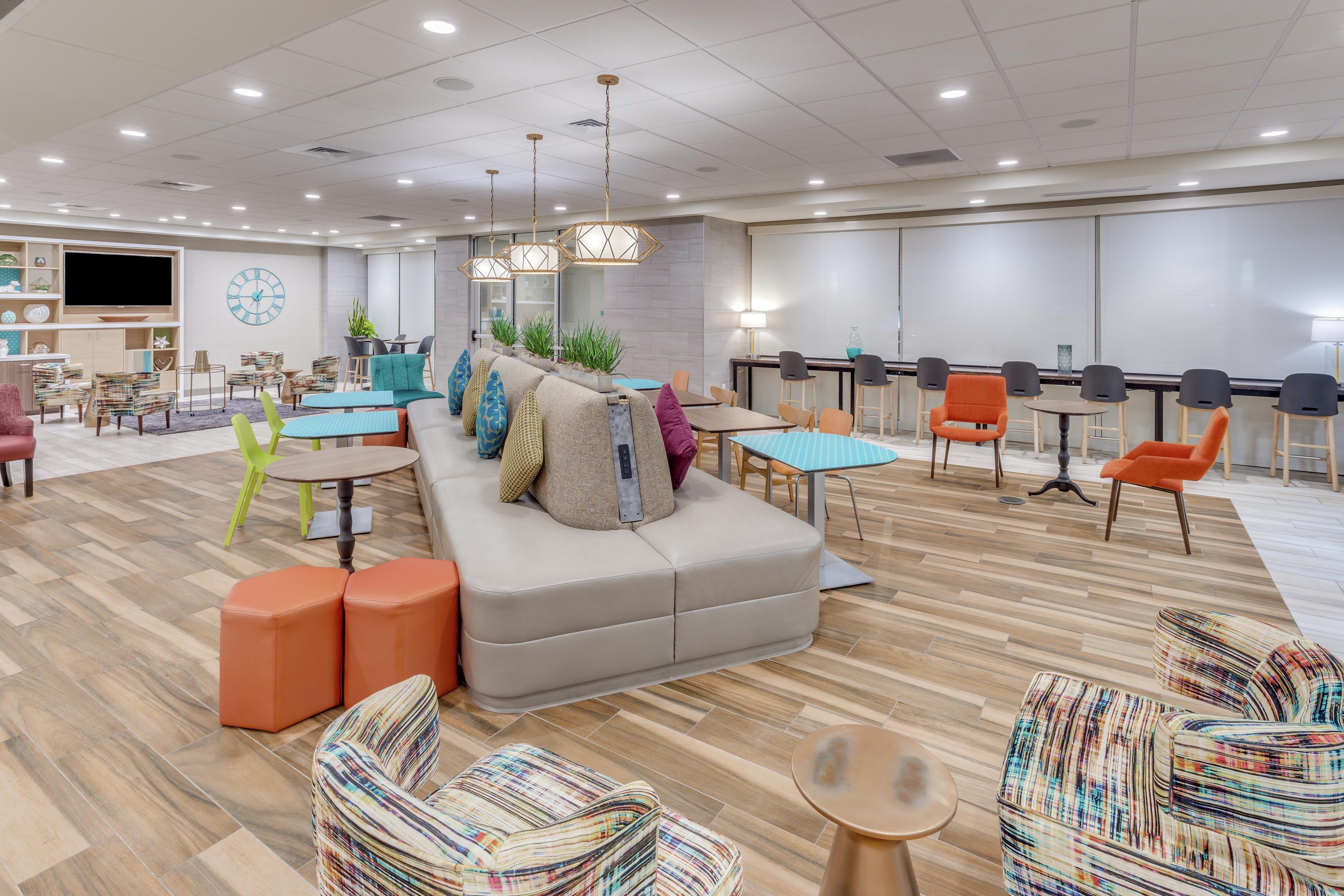 A modern hotel lobby with a large sofa, multiple tables, chairs, and a flat-screen TV.
