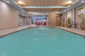 An indoor swimming pool with lounge chairs and tables, a wooden ceiling, and a view of the outside. - Home2 Suites by Hilton Indianapolis Northwest (Indianapolis)