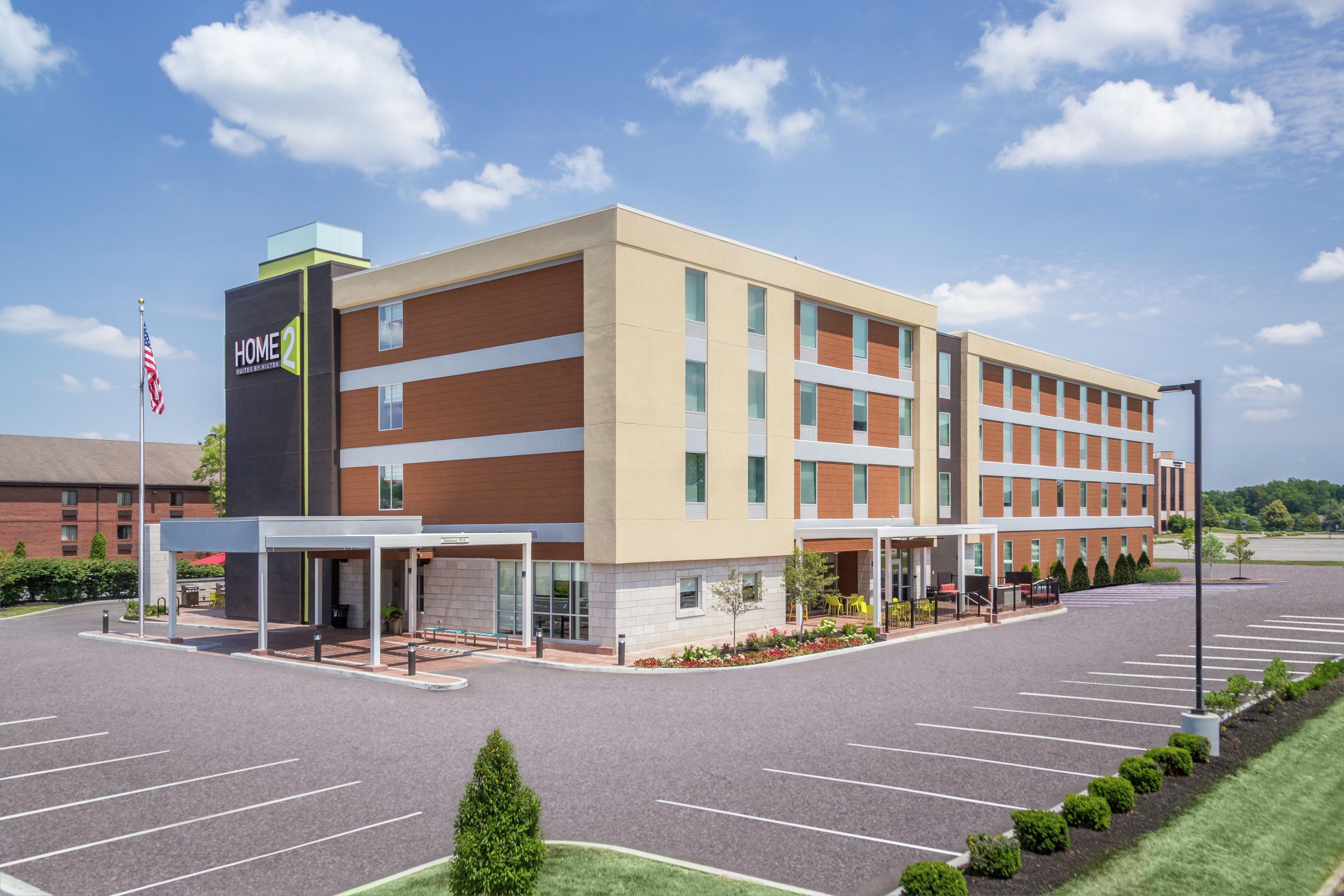 A multi-story hotel with a covered entrance, a parking lot, and a flag.