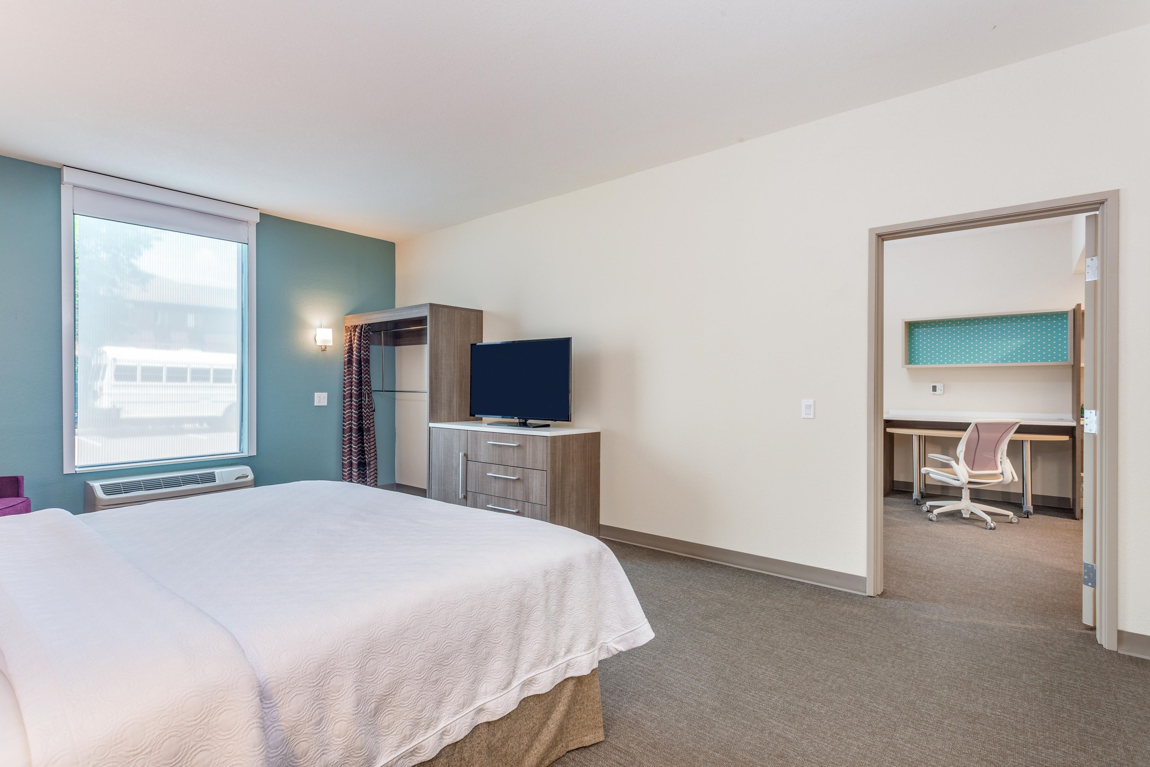 A hotel room with a bed, a desk, a television, and a window.
