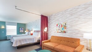 A hotel room with two beds, a sofa, a round ottoman, a lamp, and a wall with a geometric artwork. - Home2 Suites by Hilton Indianapolis Northwest (Indianapolis)
