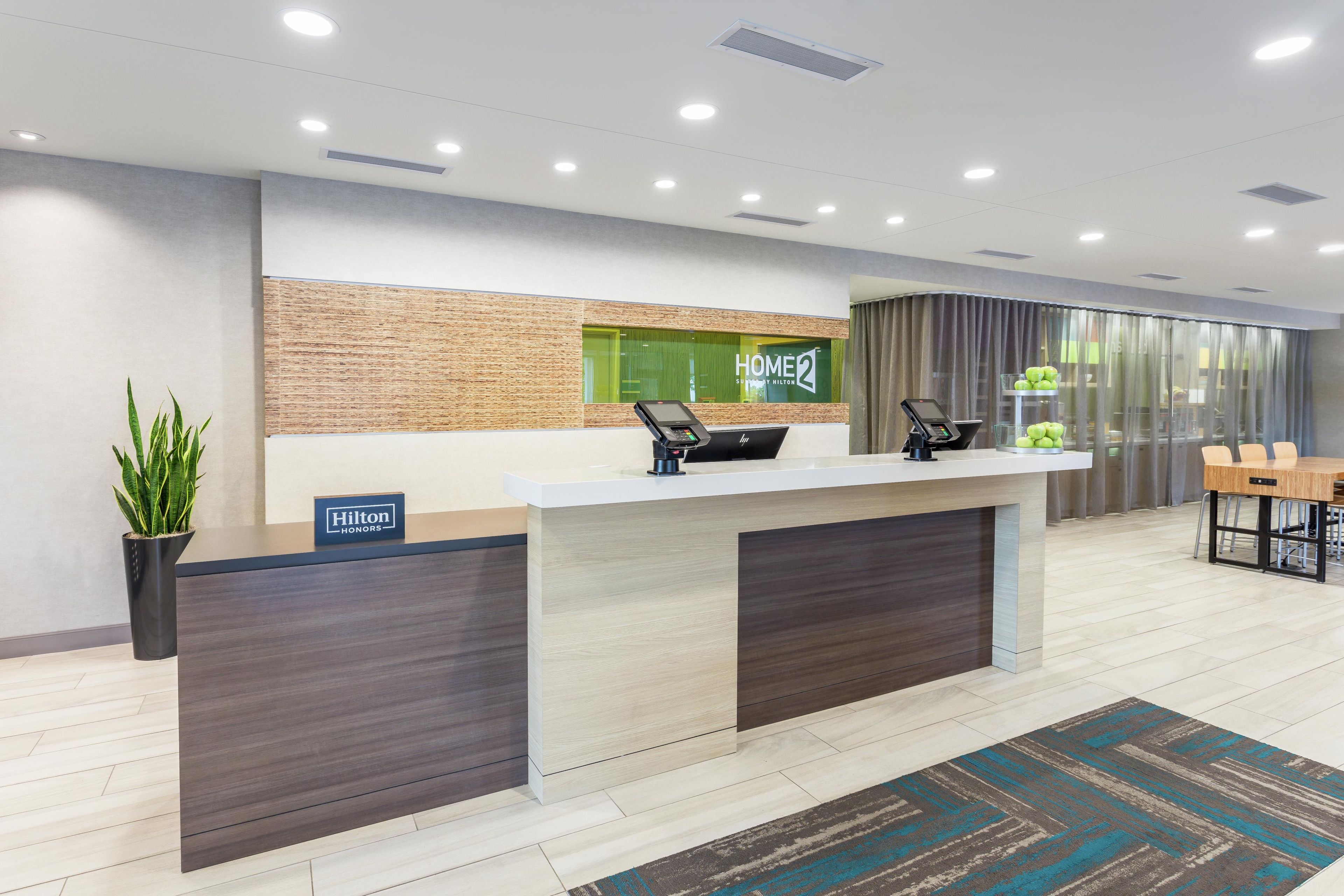 A modern hotel reception desk with a digital kiosk, a plant, and a sign indicating it's a Hilton Honors hotel.