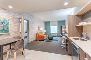 A modern hotel room with a dining area, kitchenette, and a view of the city. - Home2 Suites by Hilton Indianapolis Northwest (Indianapolis)