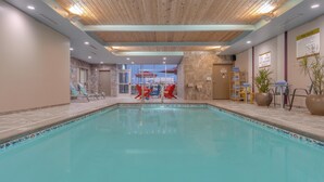 An indoor swimming pool with lounge chairs and tables, a wooden ceiling, and a view of the outside. - Home2 Suites by Hilton Indianapolis Northwest (Indianapolis)