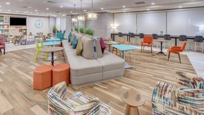 A modern hotel lobby with a large sofa, multiple tables, chairs, and a flat-screen TV. - Home2 Suites by Hilton Indianapolis Northwest (Indianapolis)