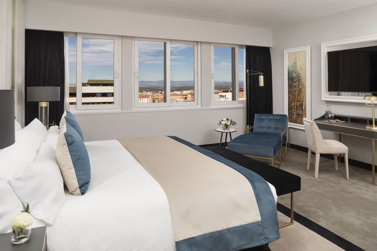 Ein Hotelzimmer mit einem großen Bett, einem Schreibtisch, einem Sessel und einem Fernseher.