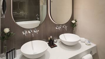 Un baño moderno con dos lavamanos grandes blancos, un espejo amplio y un florero con una rosa blanca.