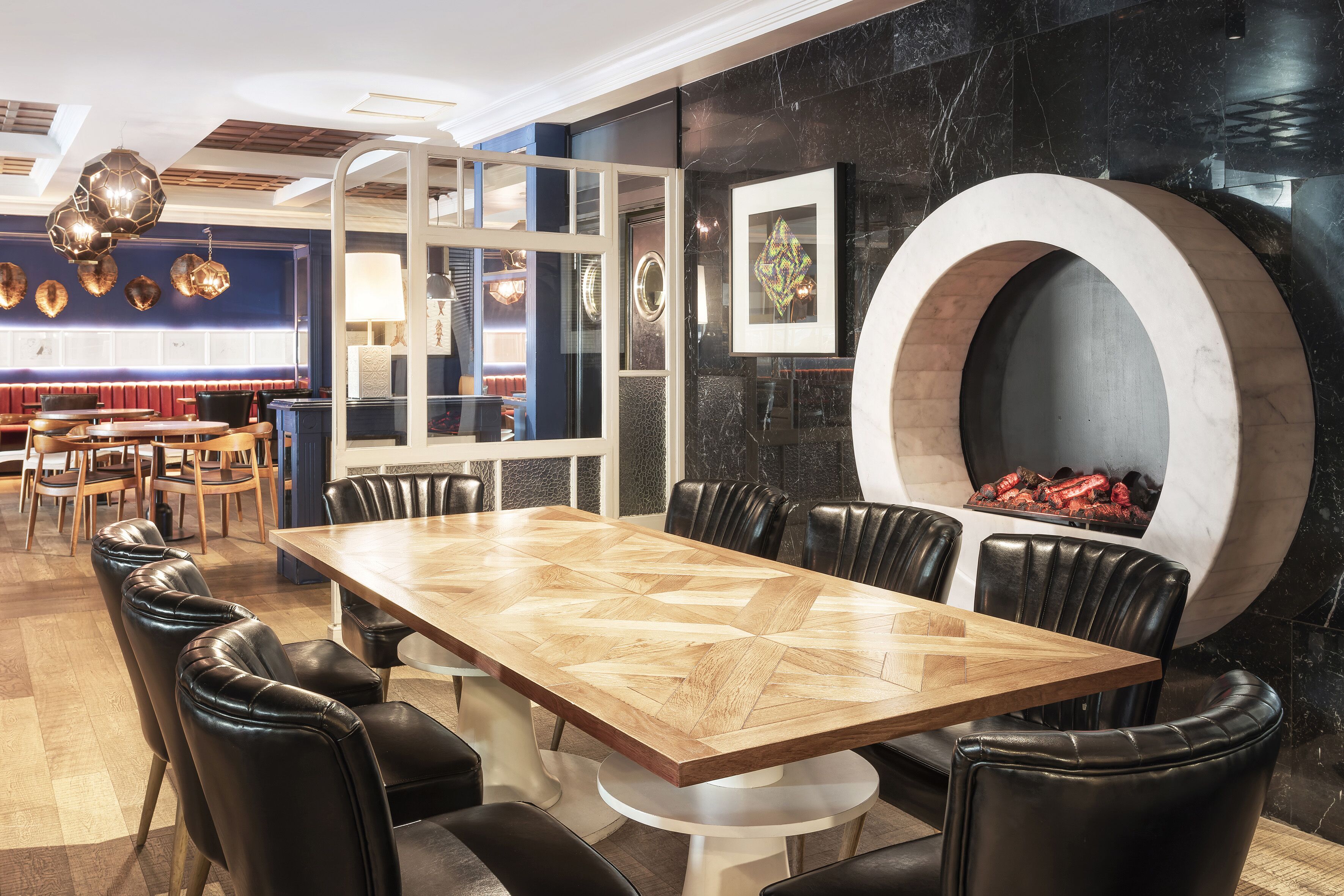 Un comedor moderno con una mesa de madera, sillas de cuero negro y una chimenea circular grande.