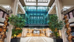 A spacious atrium with a high ceiling, large glass windows, and two ornate golden sculptures on either side. - The Level at Melia Castilla (Madrid)
