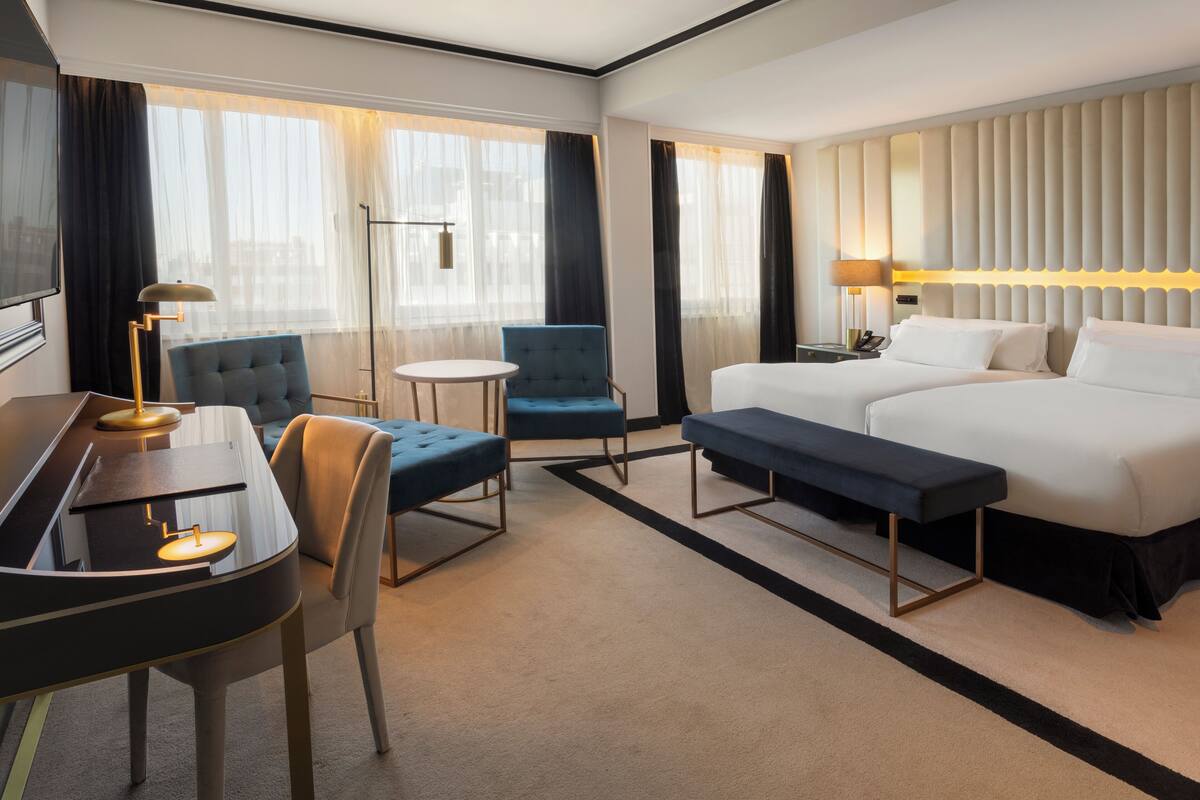 Ein Hotelzimmer mit einem Bett, einem Schreibtisch, einem Sessel, einer Bank und einem Fernseher.