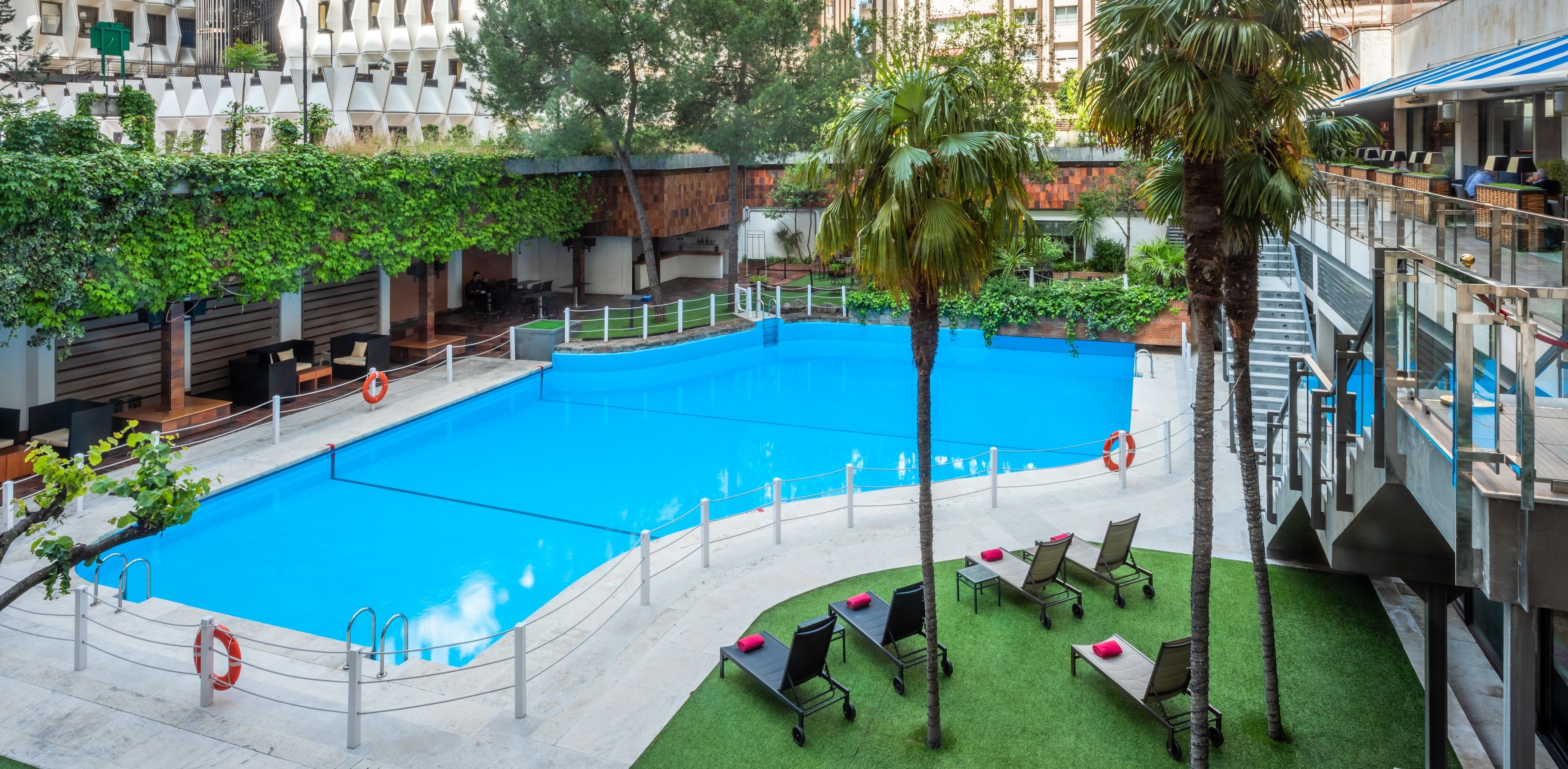 A swimming pool with a surrounding deck, lounge chairs, and a covered seating area.