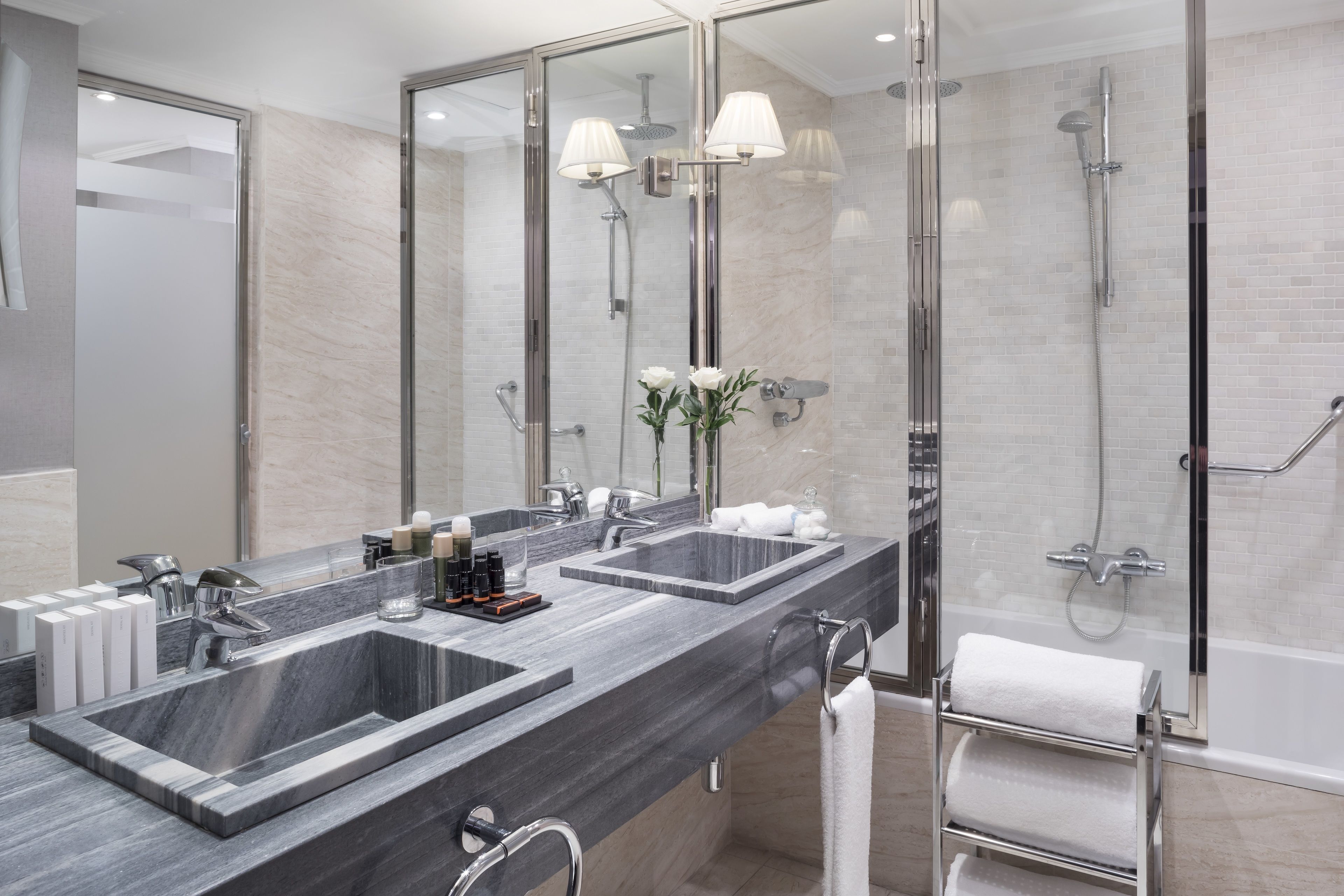 A modern bathroom with two sinks, a large mirror, and a glass-enclosed shower area.