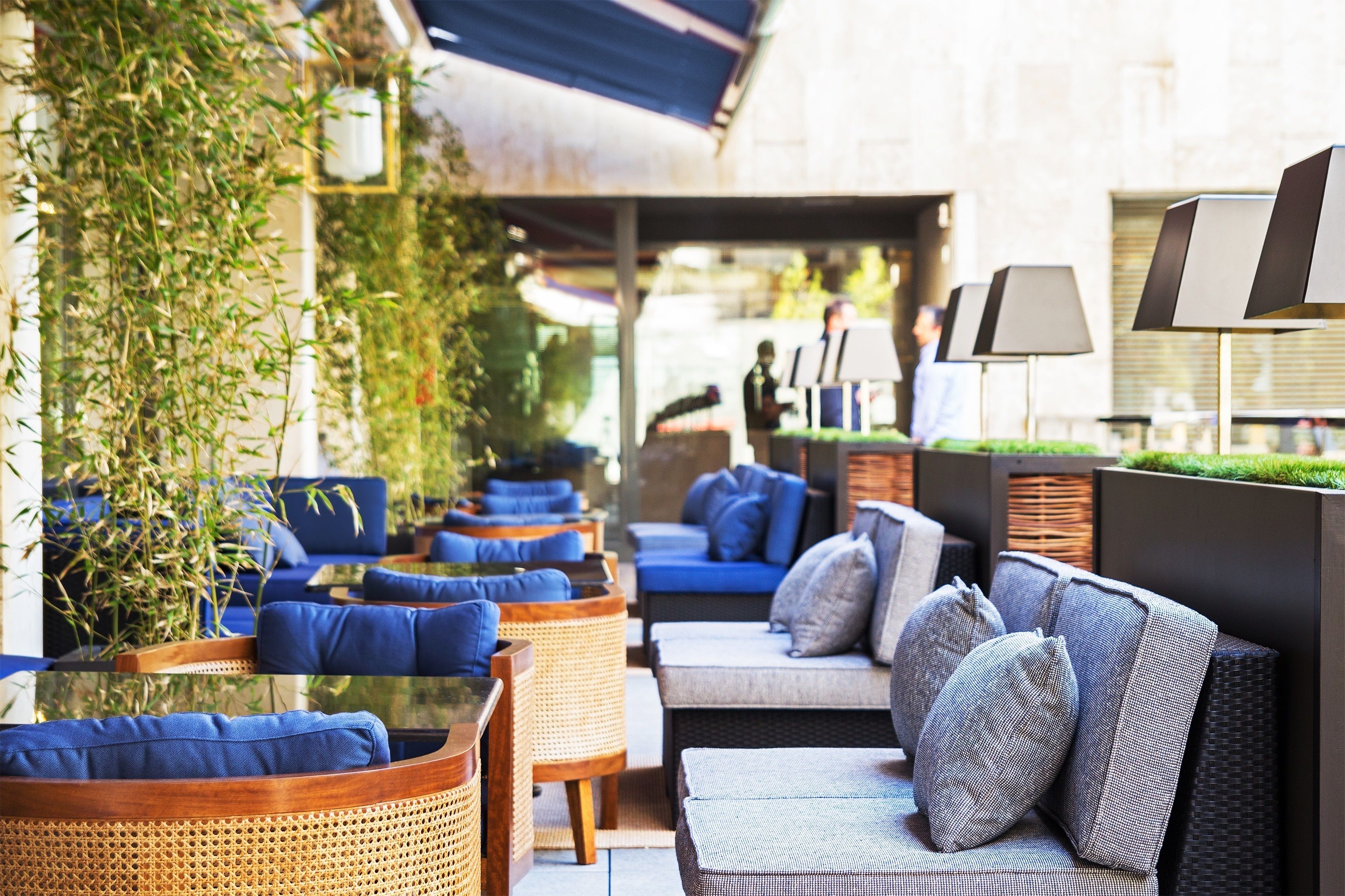 An outdoor seating area with wicker chairs and sofas, some with blue cushions, and a glass table.