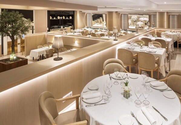 Un restaurant moderne avec des tables rondes, des chaises de couleur beige et un bar central.