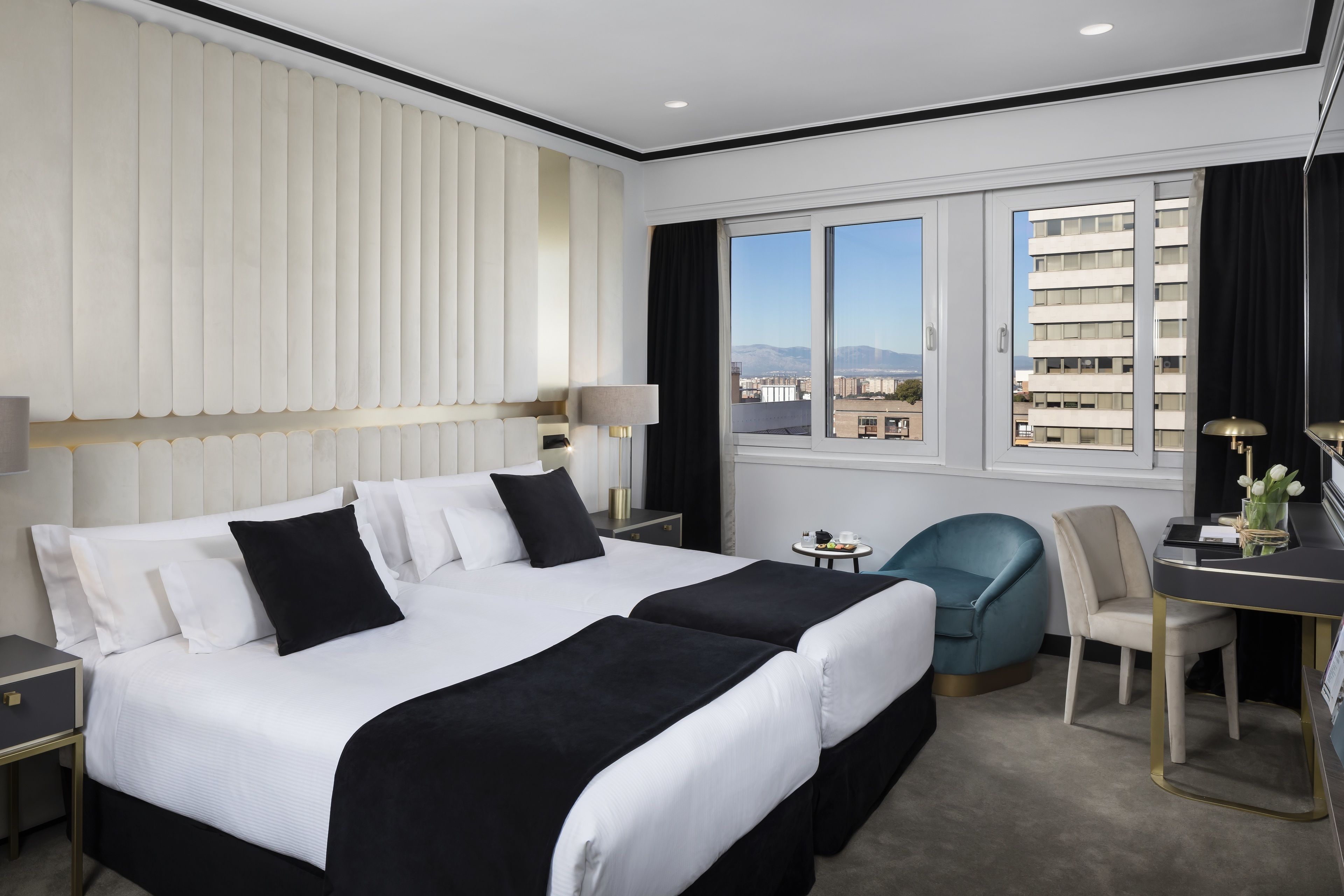 Una habitación de hotel con una cama grande, mesitas de noche, un escritorio, una silla y una ventana con vistas a la ciudad.