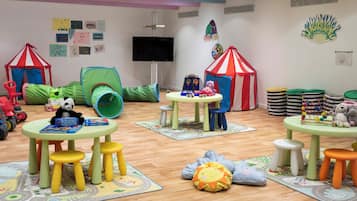 Children can play and learn in this vibrant playroom featuring a green tunnel, playhouse, and educational posters.