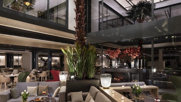 A modern hotel lobby with a central seating area, a large plant, and a fireplace. - The Level at Melia Castilla (Madrid)