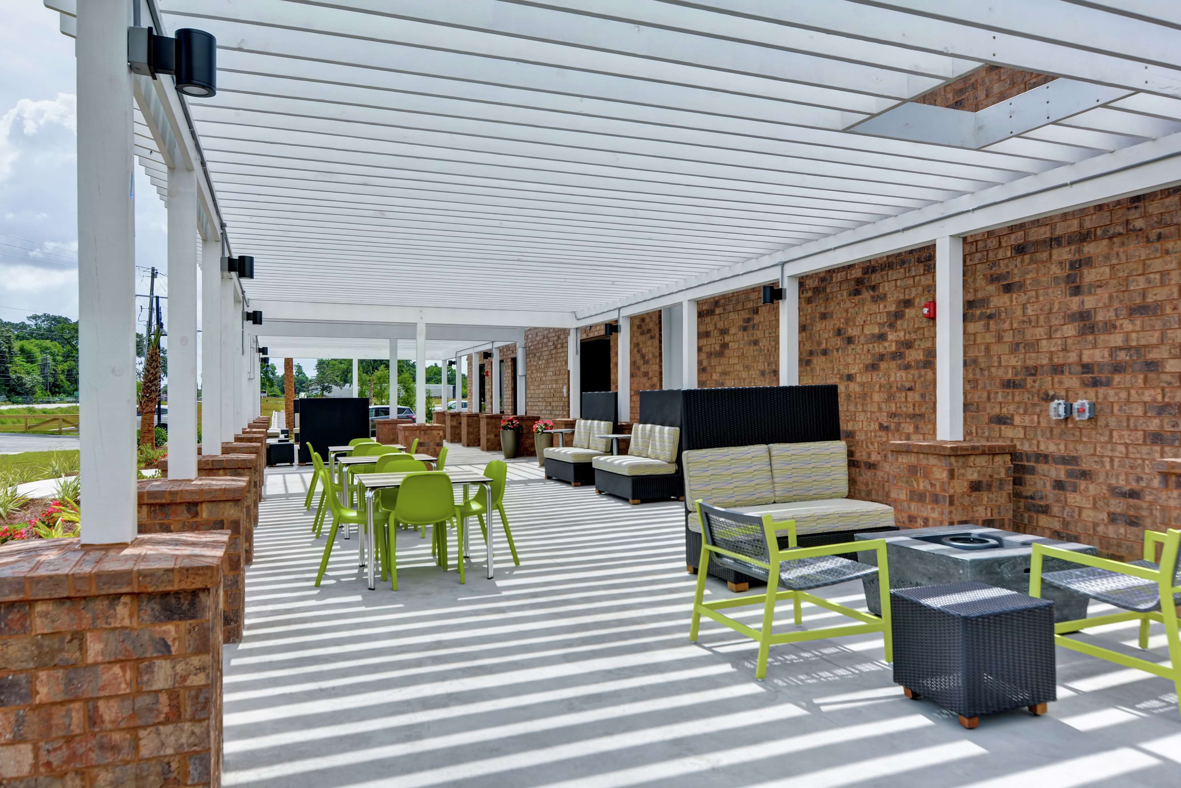Une terrasse extérieure dotée d’une pergola blanche, de murs en briques et de mobilier d’extérieur comprenant des chaises vertes, des tables et un canapé.
